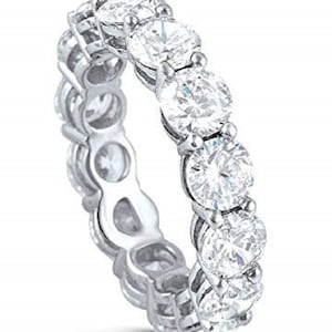May include: A silver-toned eternity band featuring a continuous row of round, clear, faceted stones set in a prong setting. The metal band has a polished finish and the stones are arranged in a single line around the entire circumference of the ring.