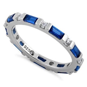 May include: Sterling silver eternity band ring with alternating blue sapphire and clear cubic zirconia stones. The ring is marked with "925" on the inside.