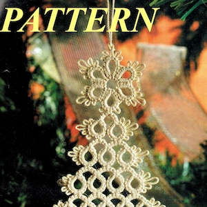 Könnte beinhalten: Ein weißer, gehäkelter Weihnachtsbaum-Anhänger mit einer Schneeflocke oben. Der Anhänger hängt an einer Schnur und befindet sich vor einem verschwommenen Hintergrund eines Weihnachtsbaums.