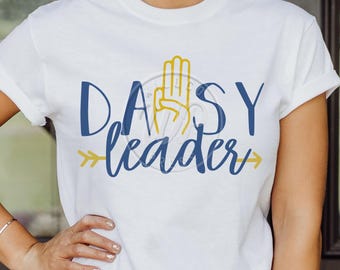 Könnte beinhalten: Weißes T-Shirt mit einem blauen und gelben Design, auf dem "Daisy Leader" mit einem Pfeil auf jeder Seite steht.