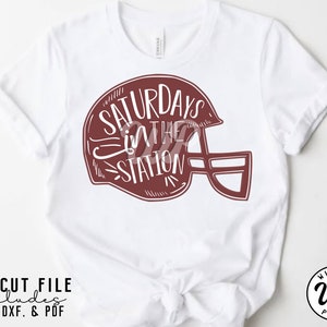 May include: White t-shirt with a maroon graphic of a football helmet with the text "Saturdays in the Station" inside the helmet.