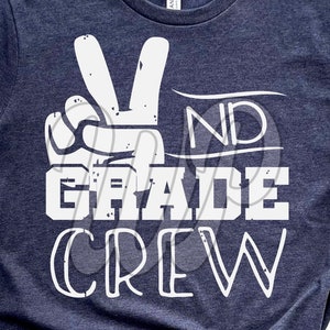 May include: A navy blue t-shirt with a white peace sign and the text "2nd Grade Crew" in a distressed font.