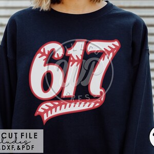 May include: A navy blue sweatshirt with a white and red baseball-themed graphic featuring the number "617" with a red baseball stitch design. The text "SVG CUT FILE includes PNG, DXF, & PDF" is at the bottom of the image.