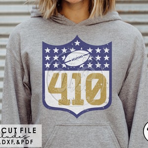 May include: Gray hoodie featuring a distressed shield design with a football, stars, and the number 410 in gold. The design is reminiscent of a sports team logo. The hoodie includes the text "SVG CUT FILE INCLUDES PNG, DXF, & PDF".