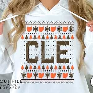 May include: White hoodie with a brown and orange Christmas jumper design featuring the letters "CLE" and snowflakes. The design also includes the state of Ohio.