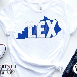 May include: A white t-shirt with a blue outline of the state of Kentucky and the word "LEX" in white letters inside the outline.