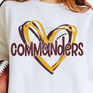 May include: White sweatshirt with a burgundy and gold heart design. The heart has a football inside and the word "Commanders" in burgundy letters.