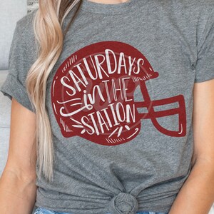 May include: Gray t-shirt with a red football helmet graphic and the text "Saturdays in the Station" in white.
