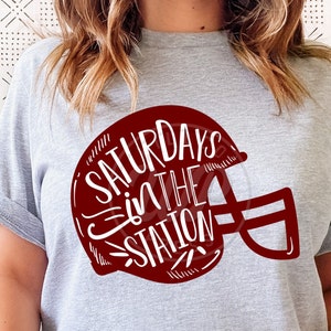 May include: A gray t-shirt with a red football helmet graphic. The helmet has the text "Saturdays in the Station" written inside.