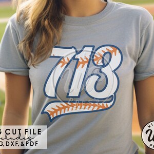 Könnte beinhalten: Ein graues T-Shirt mit einer weißen, baseball-inspirierten Nummer "713" auf der Vorderseite. Die Zahlen sind blau umrandet und haben ein Baseball-Steppdesign. Der Text "SVG CUT FILE includes PNG, DXF, & PDF" ist unten im Bild gedruckt.