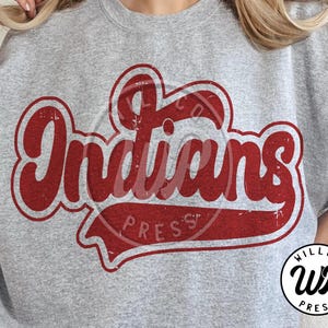 Peut inclure: Un sweat-shirt gris avec le mot "Indians" en rouge vieilli. Le texte est dans un style rétro avec un contour incurvé et une bannière en bas. Le sweat-shirt a un col rond.