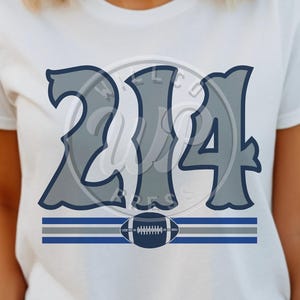 Op de afbeelding: Wit T-shirt met het nummer "214" in een gestileerd, grijs lettertype met een donkerblauwe omtrek. Daaronder een horizontaal streepontwerp met een voetbalafbeelding. Een sportartikel voor fans.