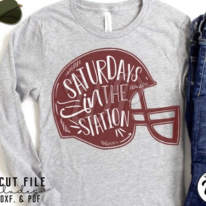 May include: A gray long-sleeve t-shirt with a maroon football helmet graphic that says "Saturdays in the Station".