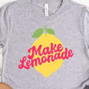 May include: Gray t-shirt with a yellow lemon graphic and the text "Make Lemonade" in pink.
