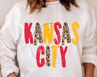 May include: White sweatshirt with the words "Kansas City" in red, yellow, and black leopard print.