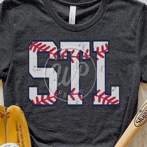 May include: A dark gray t-shirt with a white baseball-themed graphic that says "STL". The graphic has red stitching details.