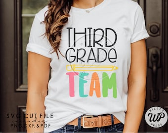 May include: A white t-shirt with the text "THIRD GRADE TEAM" in colorful letters. The text is surrounded by a yellow pencil graphic. The shirt is being worn by a person.
