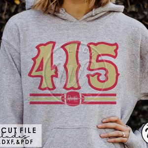 Op de afbeelding: Een grijze hoodie met een rood en gouden ontwerp met het nummer "415" en een voetbal. De tekst "SVG CUT FILE includes PNG, DXF, & PDF" staat onderaan de afbeelding.