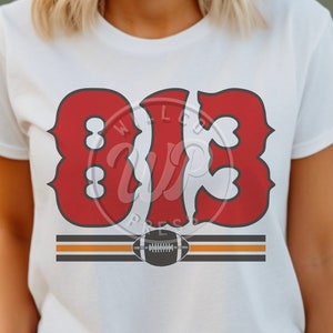 Puede incluir: Camiseta blanca con un gráfico rojo "813" y un diseño de fútbol marrón y negro.