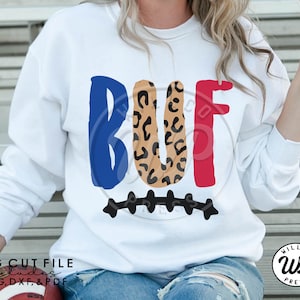 May include: White sweatshirt with a blue, brown, and red "BUF" graphic with a leopard print design. The graphic is above a black football field design.