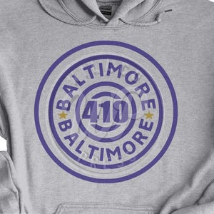 May include: Gray hooded sweatshirt with a purple circle design featuring the text "BALTIMORE" and the number "410" in the center.
