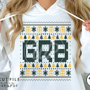 May include: A white hoodie with a green and yellow Christmas jumper design. The design features the letters "GRB" in a pixelated style. The jumper design includes Christmas trees, snowflakes, and gift boxes.