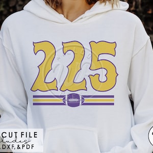 Puede incluir: Una sudadera con capucha blanca con un diseño morado y amarillo que presenta el número "225" y un gráfico de fútbol. El texto "SVG CUT FILE includes PNG, DXF, & PDF" está en la parte inferior de la imagen.