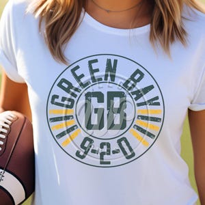 May include: White t-shirt with a green and yellow circle graphic that says "Green Bay GB 9-2-0".