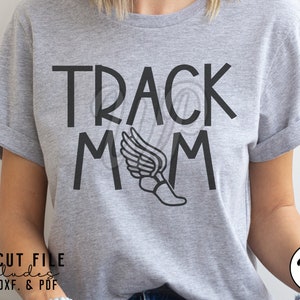 May include: Gray t-shirt with the text "TRACK MOM" in black lettering. A black silhouette of a running shoe with wings is between the "M"s.