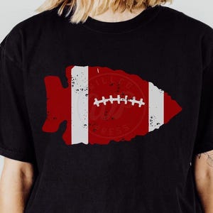 May include: Black t-shirt with a red and white football design. The football is in the shape of an arrowhead with the words "Chiefs" and "Press" inside.