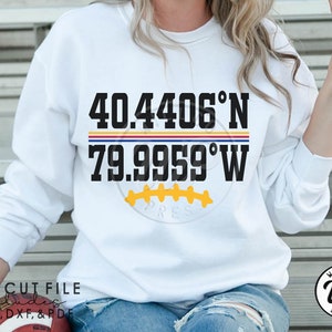 May include: White sweatshirt with black text that reads "40.4406°N 79.9959°W" with a yellow and black football graphic below the text.