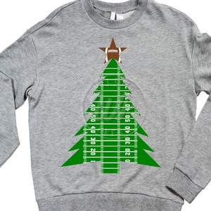 Puede incluir: Una sudadera gris con un dise&ntilde;o de &aacute;rbol de Navidad verde. El &aacute;rbol est&aacute; hecho de un campo de f&uacute;tbol con l&iacute;neas de yardas y un bal&oacute;n de f&uacute;tbol en la parte superior.