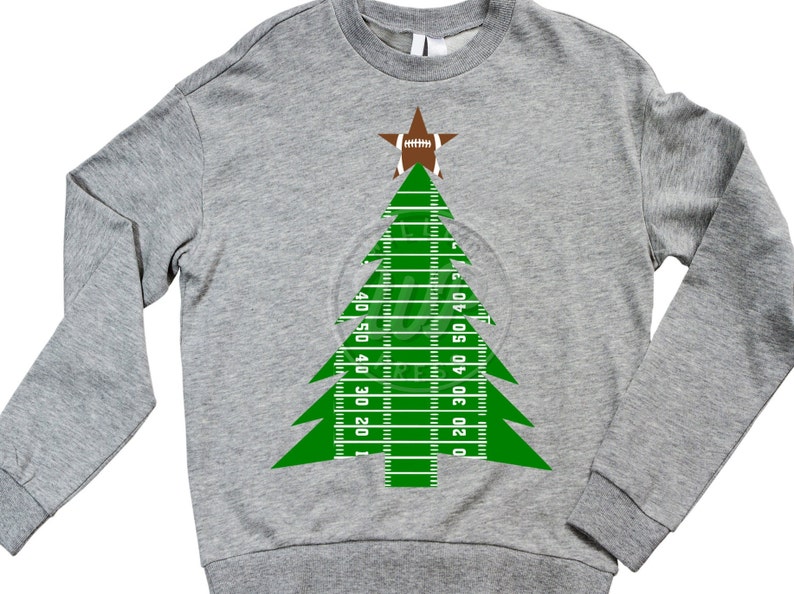Puede incluir: Una sudadera gris con un dise&ntilde;o de &aacute;rbol de Navidad verde. El &aacute;rbol est&aacute; hecho de un campo de f&uacute;tbol con l&iacute;neas de yardas y un bal&oacute;n de f&uacute;tbol en la parte superior.