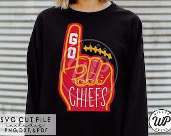 May include: Black sweatshirt featuring a red and yellow foam finger with the words "GO CHIEFS". The design includes a football and the word "CHIEFS" in white. The image also includes the text "SVG CUT FILE includes PNG, DXF, & PDF".