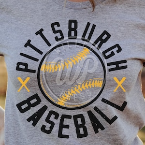 May include: A gray t-shirt with a black and yellow graphic design. The graphic features a baseball with the text "Pittsburgh Baseball" around it.