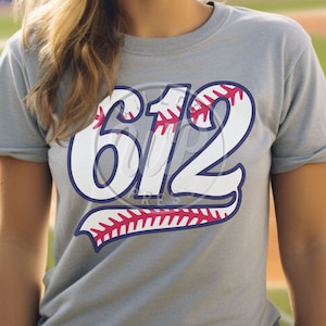 Könnte beinhalten: Ein graues T-Shirt mit der weißen Nummer "612" darauf gedruckt. Die Nummer ist blau umrandet und hat ein rotes Baseball-Steppdesign.