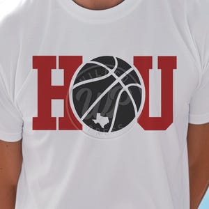 May include: White t-shirt with a red "HOU" graphic featuring a basketball with a Texas outline inside.