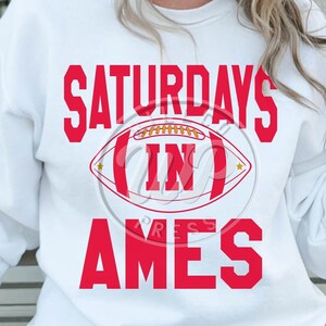 May include: White sweatshirt with red text that reads "Saturdays in Ames" with a red and white football graphic.