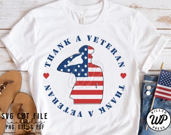May include: White t-shirt with a blue circle design that says "Thank A Veteran" with a silhouette of a person saluting in the center of the circle. The silhouette is filled with the American flag.