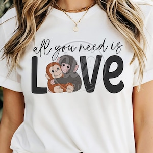 Könnte beinhalten: Weißes T-Shirt mit dem Text "all you need is LOVE" in schwarzer Schrift und Blockbuchstaben. Das "O" in LOVE wird durch eine Grafik von zwei sich umarmenden Affen ersetzt, einer braun und einer grau.
