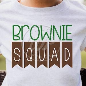 Könnte beinhalten: Weißes T-Shirt mit dem Text "Brownie Squad" in Grün und Braun. Der Text ist im Banner-Stil mit braunen Flaggen.