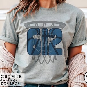 Könnte beinhalten: Ein graues T-Shirt mit einem blauen Basketball-Design, das die Nummer "612" in einem Basketballkorb zeigt. Das Design ist im Used-Look gehalten.