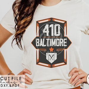 May include: A white t-shirt with a black and orange graphic design featuring the text "410 BALTIMORE" and a baseball with crossed bats. The graphic is in a vintage style with a distressed look. The text "SVG CUT FILE includes PNG, DXF, & PDF" is at the bottom of the image.