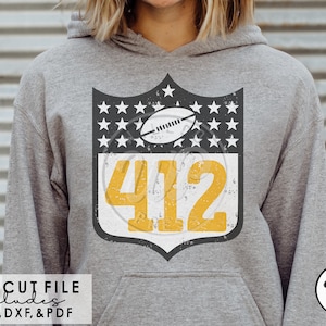 May include: A gray hoodie with a black and white shield design featuring a football and the number 412. The shield has a distressed look and is surrounded by white stars.