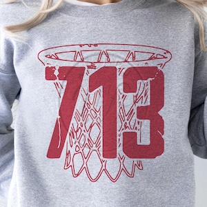 Puede incluir: Sudadera gris con un aro de baloncesto rojo y el número 713 impreso en ella.