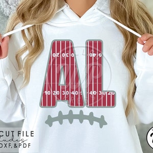 May include: White hoodie with a red and gray design of the letters "AL" with football field yard lines. The letters are outlined in gray and the yard lines are red. The design also includes a gray football stitch design below the letters.