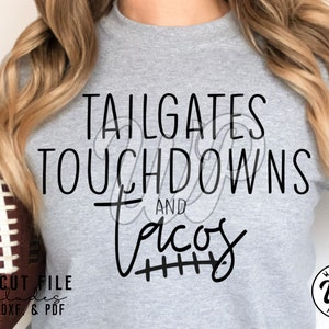 May include: A gray t-shirt with the text "TAILGATES TOUCHDOWNS AND Tacos" in black lettering. The word "Tacos" has a football field design underneath it.