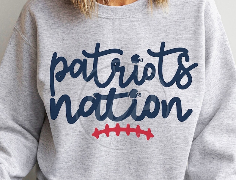 May include: Gray sweatshirt with the text "patriots nation" in blue lettering. There are two football helmet graphics above the text and a red football stitch design below the text.