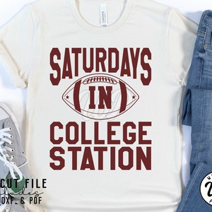Puede incluir: Una camiseta blanca con texto marr&oacute;n que dice "Saturdays in College Station" con un gr&aacute;fico de f&uacute;tbol marr&oacute;n. El texto "SVG Cut File includes PNG, DXF & PDF" est&aacute; en la parte inferior de la camiseta.