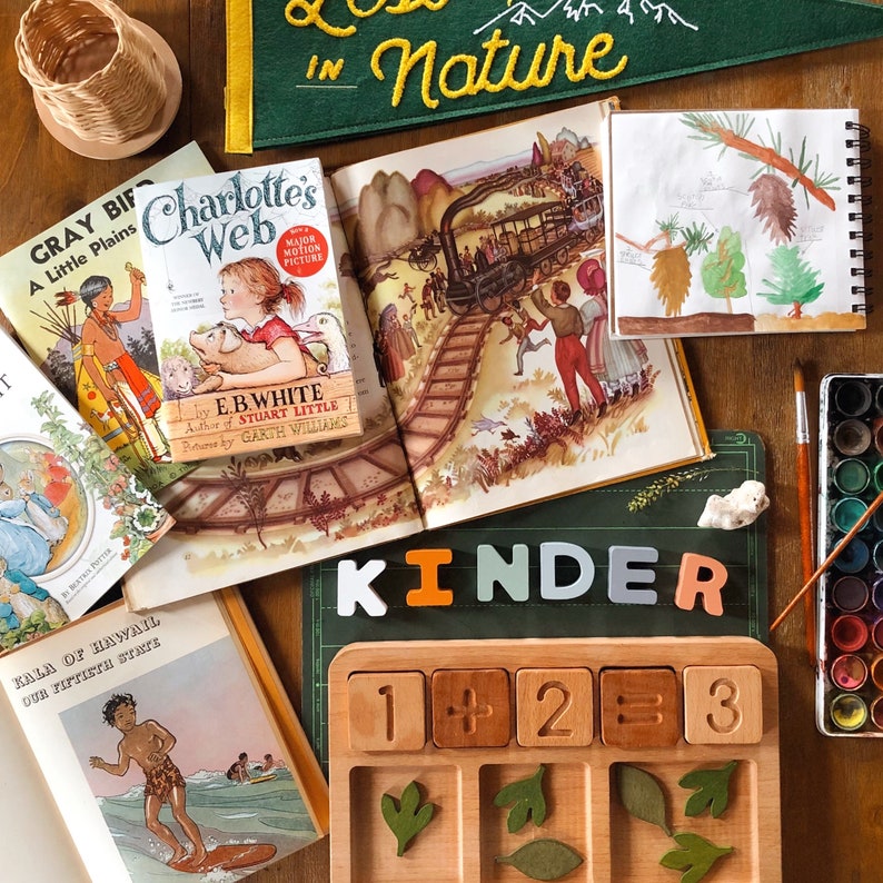 May include: A wooden counting board with numbers 1, 2, and 3, plus and equals signs. The board has five slots with leaves in each slot. The board is on a green surface with the word "kinder" in white, orange, light blue, and pink letters.